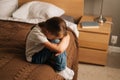 Top view of upset little girl hugging knee, sobbing with head bowed and crying sitting alone on bed in bedroom. Royalty Free Stock Photo