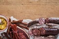 Top view of various sausages and smoked lard on a paper near a bowl of hummus on a wooden surface