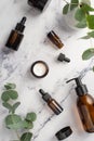 Top view vertical photo of glass bottles with natural cosmetics jar with cream and vase with eucalyptus on white marble background