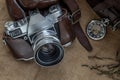 Top view of a vintage photo camera and a brown leather bag with scarf and pocket watch on sack cloth background Royalty Free Stock Photo