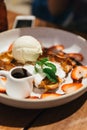 Top view of waffle topping with a scoop of vanilla ice cream, whip cream, sliced strawberry, mint leaves and chocolate sauce.