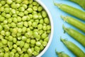 A top view of a white bowl with a crop of green peas, next to not cracked pods. Royalty Free Stock Photo