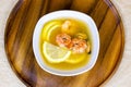 Top view of white bowl with traditional light spicy thai cuisine tom yam soup with shrimps, seafood and lemon on wooden board
