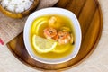 Top view of white bowl with traditional light spicy thai cuisine tom yam soup with shrimps, seafood and lemon on wooden board