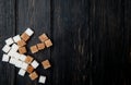 top view of white and brown sugar cubes scattered on dark wooden background with copy space