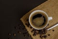 Top view of a white ceramic cup of black Americano hot coffee on sackcloth and a dark background with a pile of roasted coffee Royalty Free Stock Photo