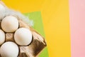 Top view of white chicken eggs with feather in an open egg carton on colorful background. Copy space. Natural healthy food and Royalty Free Stock Photo