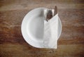 Top view of white circle plate with spoon, fork, knife and napkin on wooden table Royalty Free Stock Photo