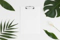 Top view of a white clipboard mockup with tropical leaves decoration