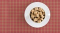 Top view of white coffee or tea cup full brown sugar cubes on red squared background. Diet unhealty sweet addiction