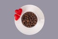Top view of white cup with grains of coffee.Two red hearts lying on a saucer next to the cup.View from above.Flat lay.Grey