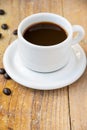 Top view of white cup and plate with coffee, on wooden table with coffee beans, in vertical, Royalty Free Stock Photo