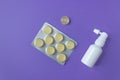 Top view of white ear spray bottle and blister of yellow cough drops. Purple background. Health care in the spring time