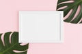 Top view of a white frame mockup with monstera leaf decoration on a pink background. Landscape orientation