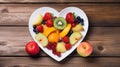 Top view on white heart shaped bowl of healthy fresh fruit salad on a wooden background. View from above. Apple