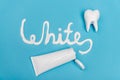 Top view of white lettering near tube of toothpaste and tooth model on blue background.
