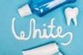 Top view of white lettering from toothpaste, tooth model and mouthwash on blue background.