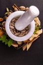 Top view of white mortar pestle crushing brown tablets with scattered whole spices and herbs on a black background. Ayurveda