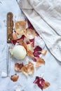 Top view of white onion with onion peelings and a knife and kitchen towel on a white surface