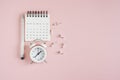 White opened calendar, analog alarm clock, pen and thumbtacks on sweet pink background