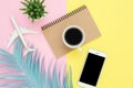 Top view of white paper notebook, pen, mock up smartphone, blue leaf, coffee and plane on pink yellow pastel color. Royalty Free Stock Photo