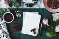 Top view of white paper sheets, coffee, rose, stamps, cake, camera on a green background