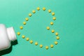 Top view of a white pill bottle and yellow pills forming a heart shape on the green surface