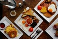 Top view of the white plates with tasty breakfast meals, spices, and cutlery on a wooden table