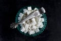 Top view on white sugar cubes in turquoise glass vase / sugar-bowl with vintage silver sugar tweezers on dark surface