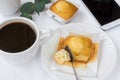 Top view of white table surface, cup of coffee, muffin on plate, smartphone, eucalyptus branch, styled image for social media