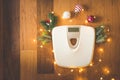 Top view of a white weight scale with Christmas decorations and lights on wooden background Royalty Free Stock Photo