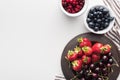 Top view of whole cranberries and blueberries on bowl, strawberries and cherries on plate.