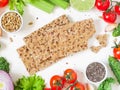 Top view of whole grain rye crispbreads surrounded fresh vegetables, greens and seeds over white background.