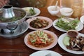 A top view of a wide variety of Thai food including Papaya Salad, Tom Yum Hot Pot, Roasted Pork, Roasted Chicken