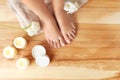 Top view of woman with beautiful feet, candles, flowers and moisturizing cream on wooden floor. Spa treatment Royalty Free Stock Photo