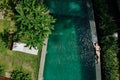 Top view of woman in beige bikini relaxing on edgeof infinity pool around palm trees and jungle. Luxury holiday.Girl Royalty Free Stock Photo