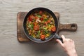 Top view of woman cooking omelet with mushrooms, tomatoes and greens on frying pan on wooden board. Royalty Free Stock Photo