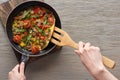 Top view of woman cooking omelet with mushrooms, tomatoes and greens on frying pan with wooden shovel. Royalty Free Stock Photo