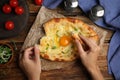 Top view of woman eating delicious Adjarian khachapuri at wooden table, closeup