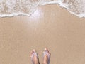 Top view of woman feet wear slippers standing on the sand, female tourist on the beach in the sunny day