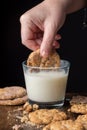 Top view of woman hand with chocolate chip cookie in glass of milk, on wooden table with cookies and crumbs, selective focus, with Royalty Free Stock Photo