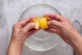 Top view of woman hand cracking raw brown egg into glass bowl on the marble surface