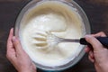 Top view of woman hand mixing with whisk dry ingredients and batter on wooden background