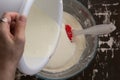 Top view of woman hand pouring whisked eggs into swollen semolina batter as ingredient for baking mannik caressole on the brown