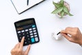 Top view of woman hand putting coin in piggy bank while using calculator on white desk at home. Family expense, savings, collect Royalty Free Stock Photo