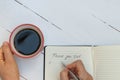 Top view of woman hand writing thank you list and holding cup of coffee on white wooden table