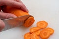 Top view of woman hands cutting raw carrots into round slices using a knife on a white background Royalty Free Stock Photo