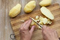 Top view of woman hands cutting scrubbed boiled potatoes in jackets using knife on the wooden background