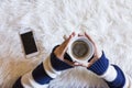 Top view of woman hands holding a cup of coffee over white background. Smarth phone besides. Lifestyles Indoors. Royalty Free Stock Photo