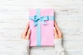 Top view woman hands holding present box with colored bow on white rustic wooden background with copy space Royalty Free Stock Photo
